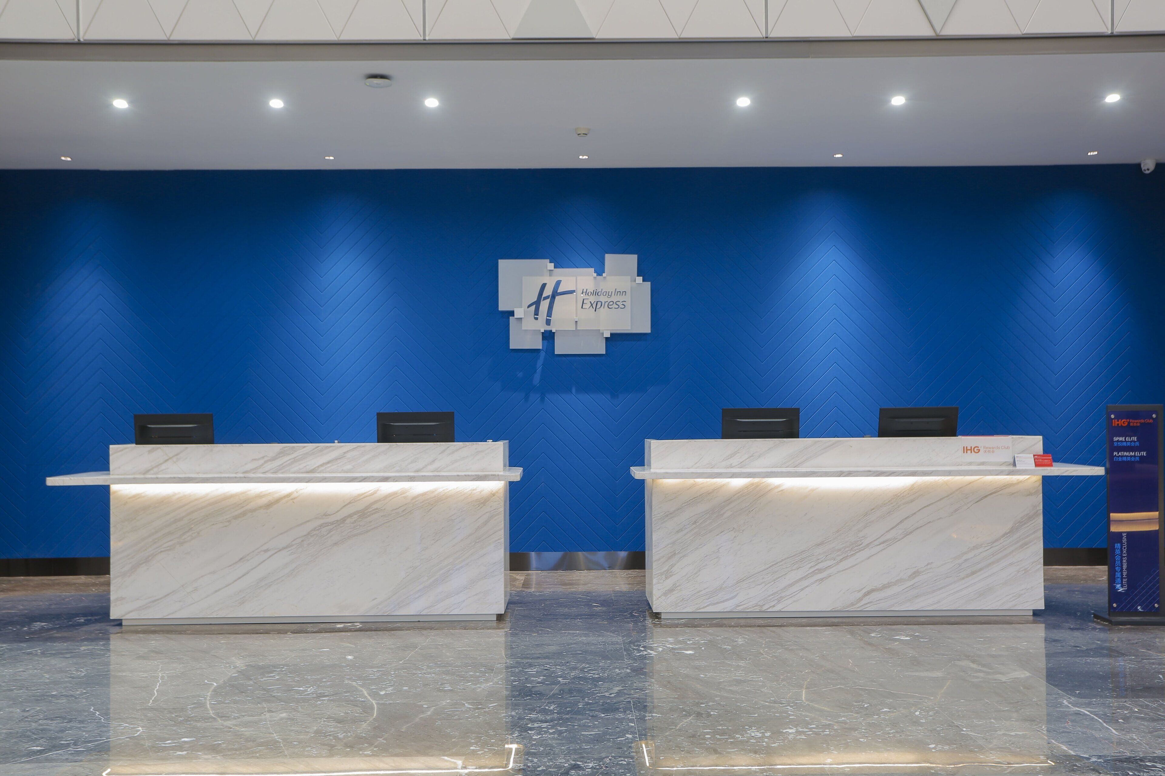 A reception area with two marble reception desks, a blue wall with a Holiday Inn Express logo, and a blue wall with a herringbone pattern.