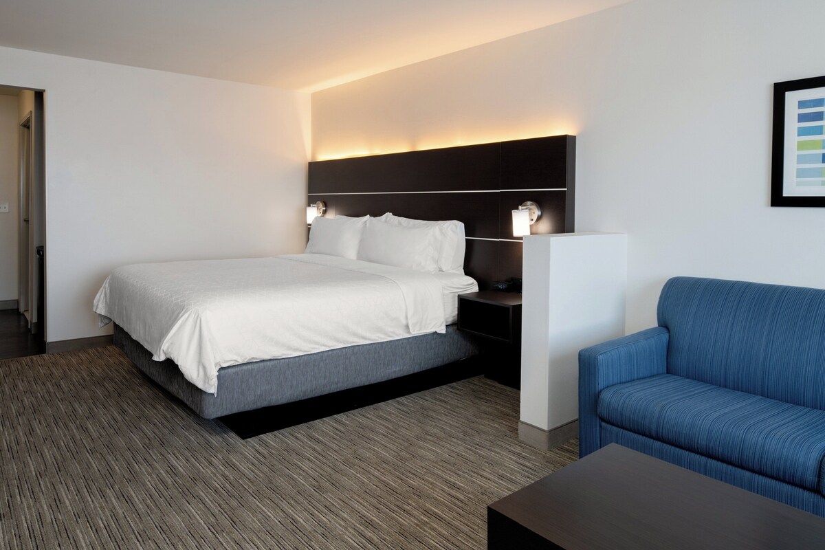 A modern hotel room with a large bed, a blue sofa, and a nightstand with a lamp.