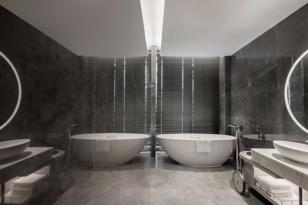 Un baño moderno con dos tinas independientes de gran tamaño, una ducha central y un tocador con lavamanos y espejo.