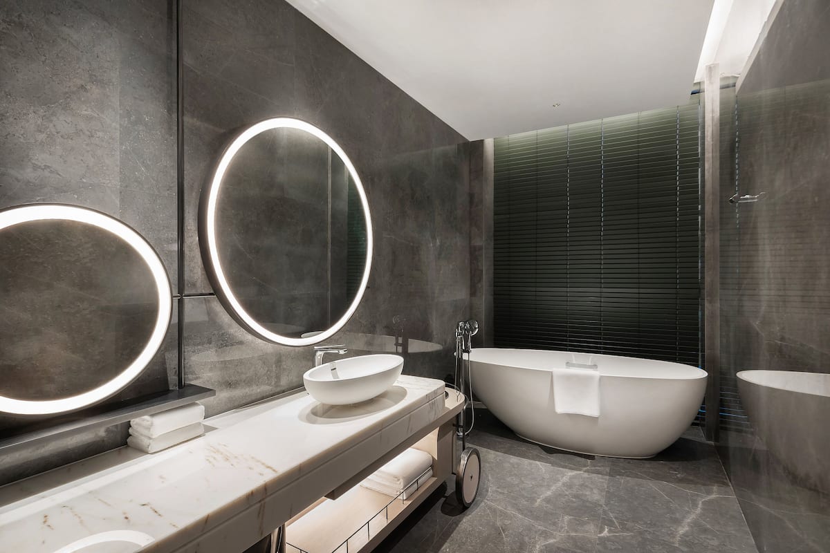 Un baño moderno con una bañera independiente grande, un espejo redondo con luz y una encimera de mármol.