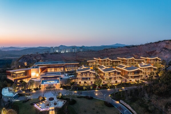 A hotel with multiple buildings, a well-maintained lawn, and a view of distant mountains. - Hotel Indigo Nanjing Garden Expo by IHG (Nanjing)