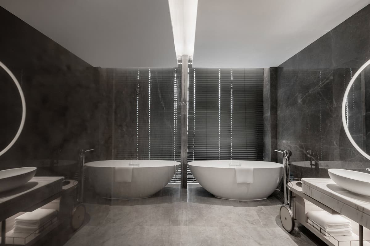 Un baño moderno con dos tinas independientes de gran tamaño, una ducha central y un tocador con lavamanos y espejo.