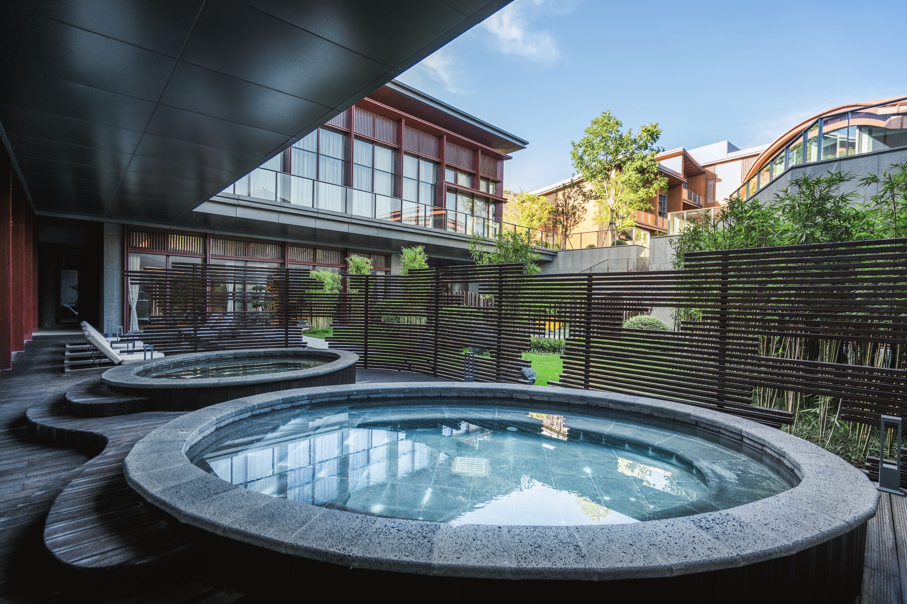Un espace spa moderne doté de trois bains à remous disposés en demi-cercle, entouré d’une terrasse en bois et d’une clôture en bambou.