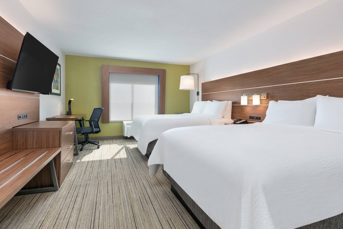 A hotel room with two beds, a desk, a chair, a TV, and a window.