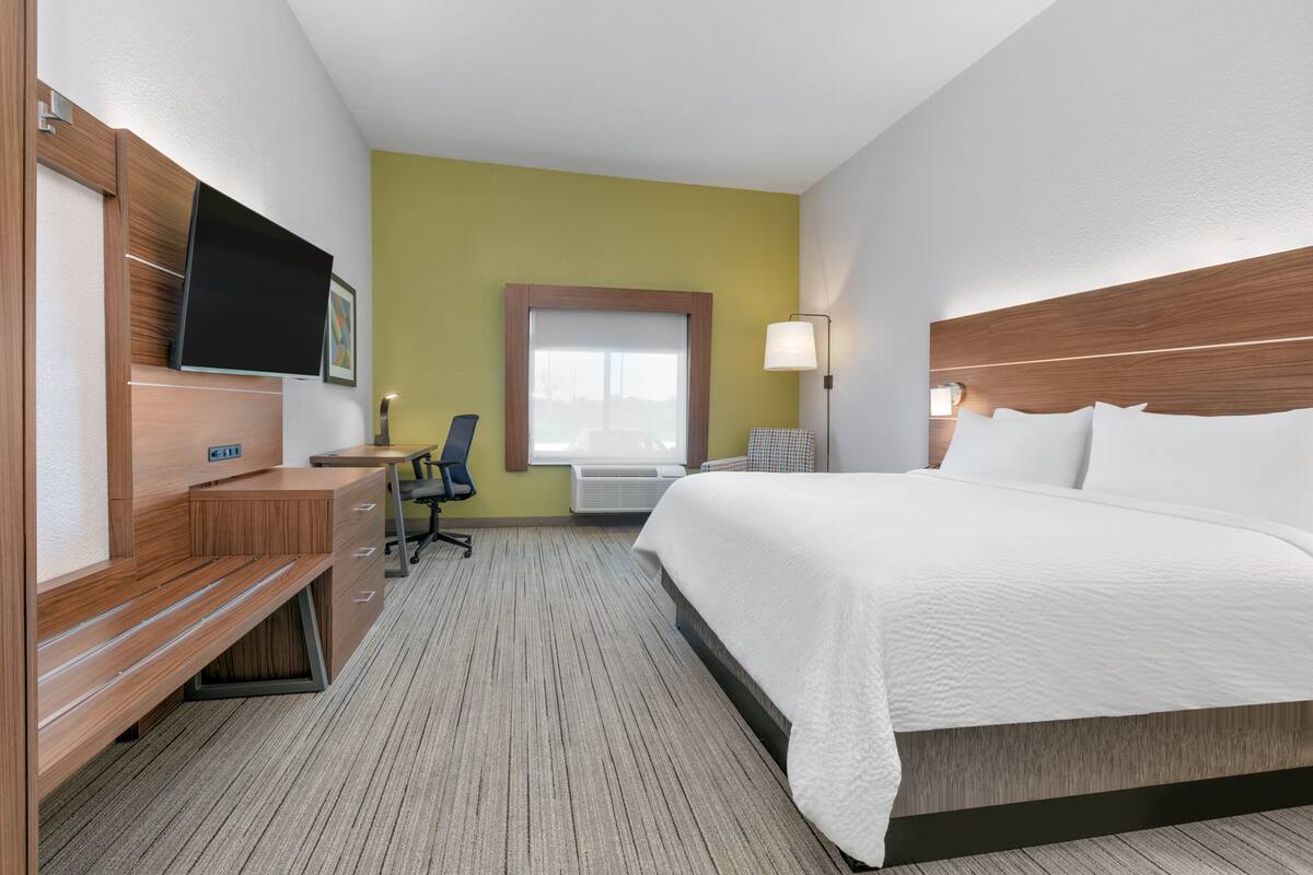 A hotel room with a bed, desk, chair, TV, window, and lamp.