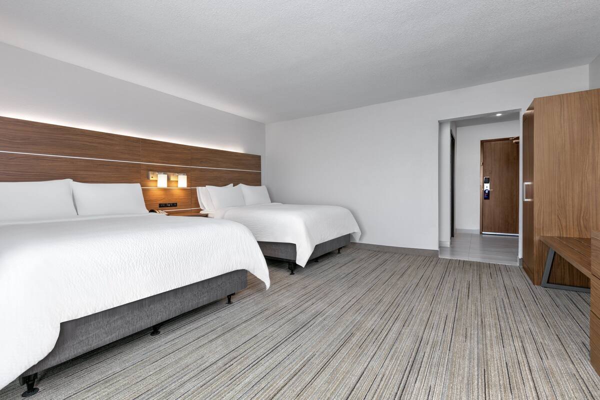 A hotel room with two beds, a wooden headboard, a nightstand, and a wardrobe.