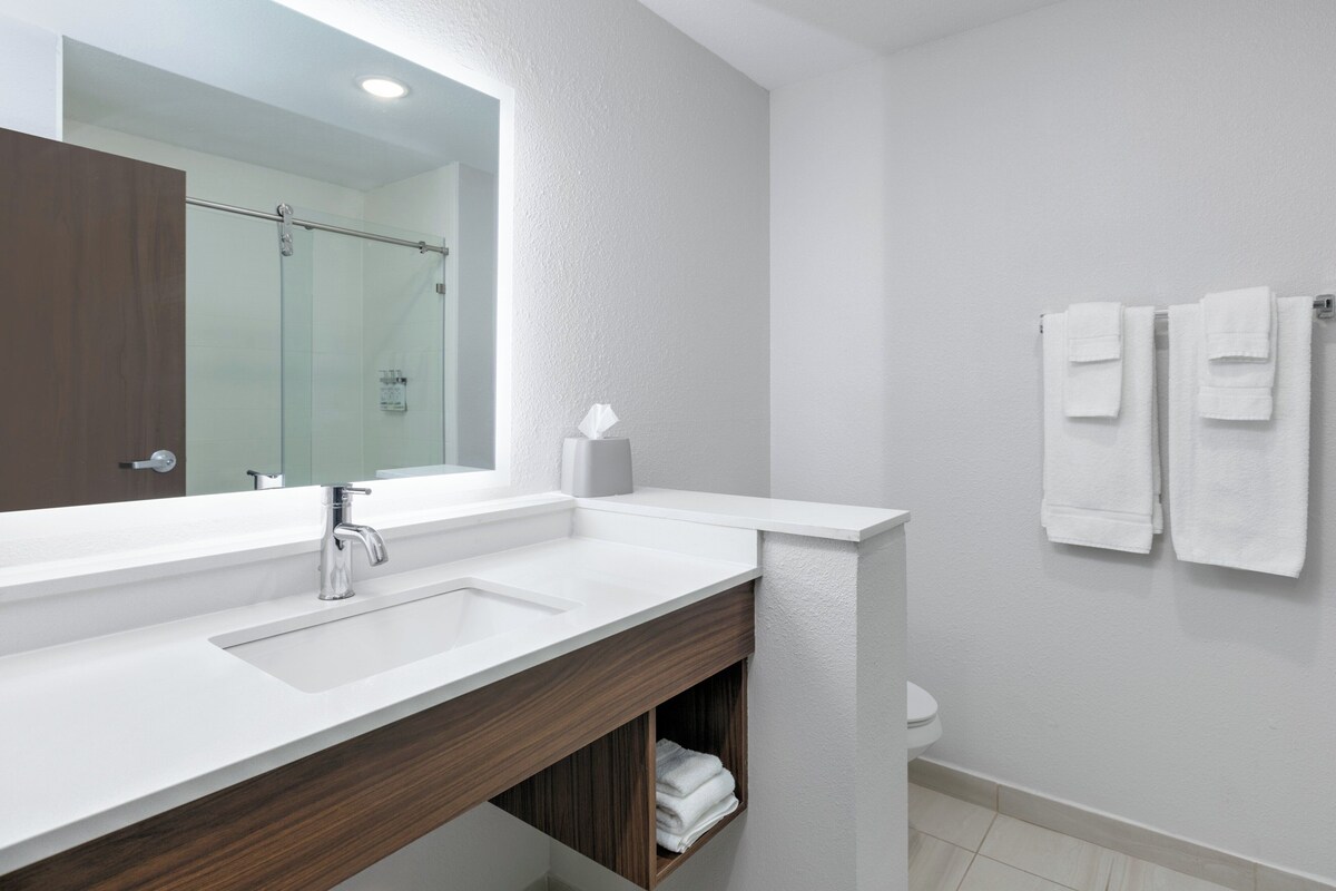 Un baño moderno con un espejo grande, dos lavamanos, un mueble de tocador de madera, un inodoro y dos toallas colgadas en la pared.