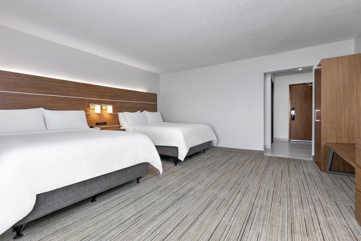 Habitación de hotel con dos camas, cabecero de madera, mesita de noche y armario.
