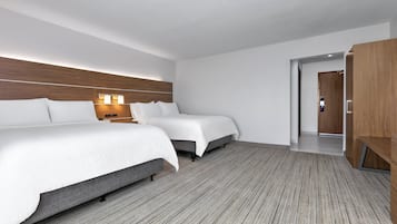 A hotel room with two beds, a wooden headboard, a nightstand with a lamp, and a wardrobe.