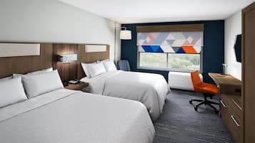A hotel room with two beds, a desk, an orange chair, and a window with a view.