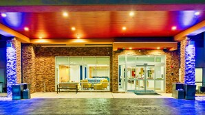 A hotel entrance with a stone facade, glass doors, and a seating area with yellow chairs and a bench. - Holiday Inn Express & Suites Harrisonburg University Area by IHG (Harrisonburg)