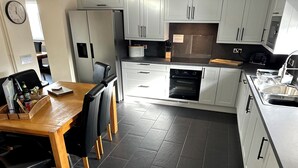 Eine moderne Küche mit weißen Schränken, einem eingebauten Ofen und einer Essecke mit Holztisch und Stühlen.