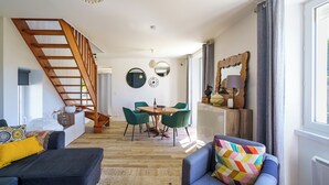 Un vaste espace de vie agrémenté d’un escalier en bois, d’une table à manger avec des chaises et d’un coin salon confortable avec un coussin aux couleurs vives.