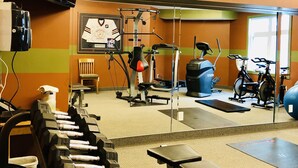 A gym with exercise equipment, a bench, and a wall-mounted TV. - A Small Hotel Room for Mountain Lovers (Canmore)