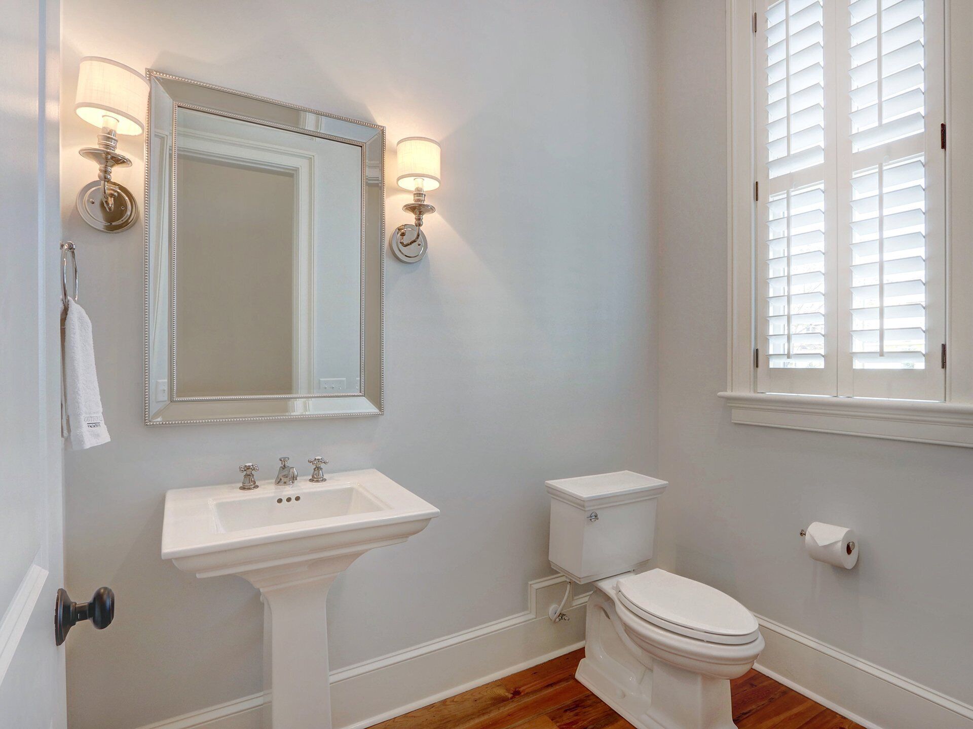 Une salle de bain avec un lavabo sur colonne, des toilettes et un grand miroir agrémenté d’appliques murales.