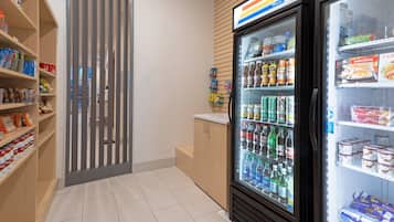 Un refrigerador exhibe diversas bebidas y aperitivos, junto a un mueble de madera y una presentación vertical de productos envasados.