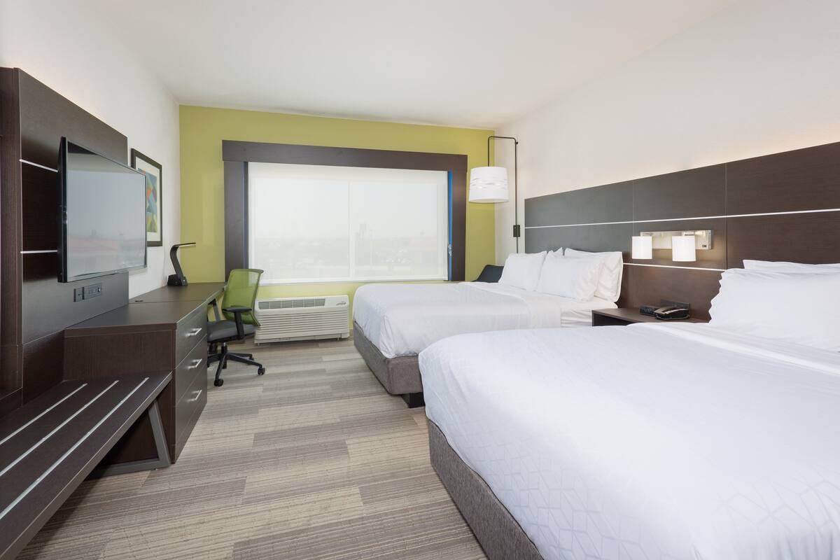 A hotel room with two beds, a desk, a flat-screen TV, a chair, and a large window.