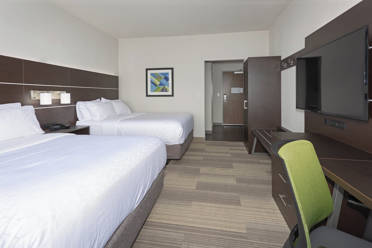 A hotel room with two beds, a desk, a chair, a TV, and a door leading to a bathroom.