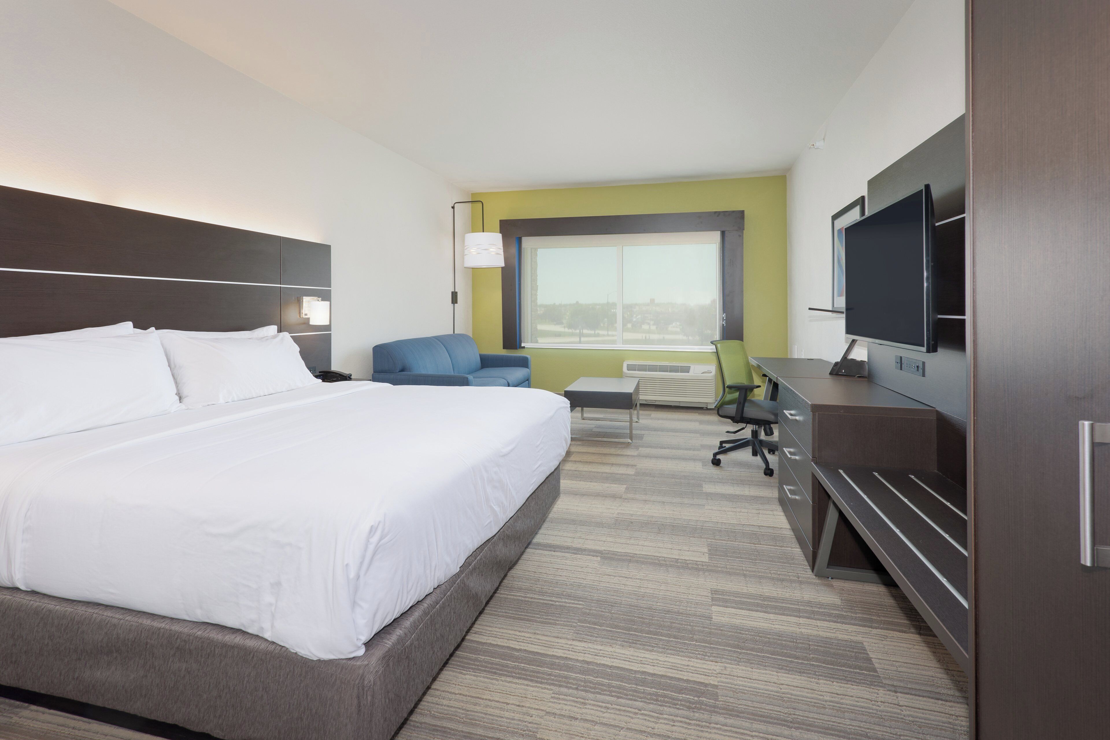 Habitación de hotel con una cama grande, un escritorio con computadora, una silla y un televisor.