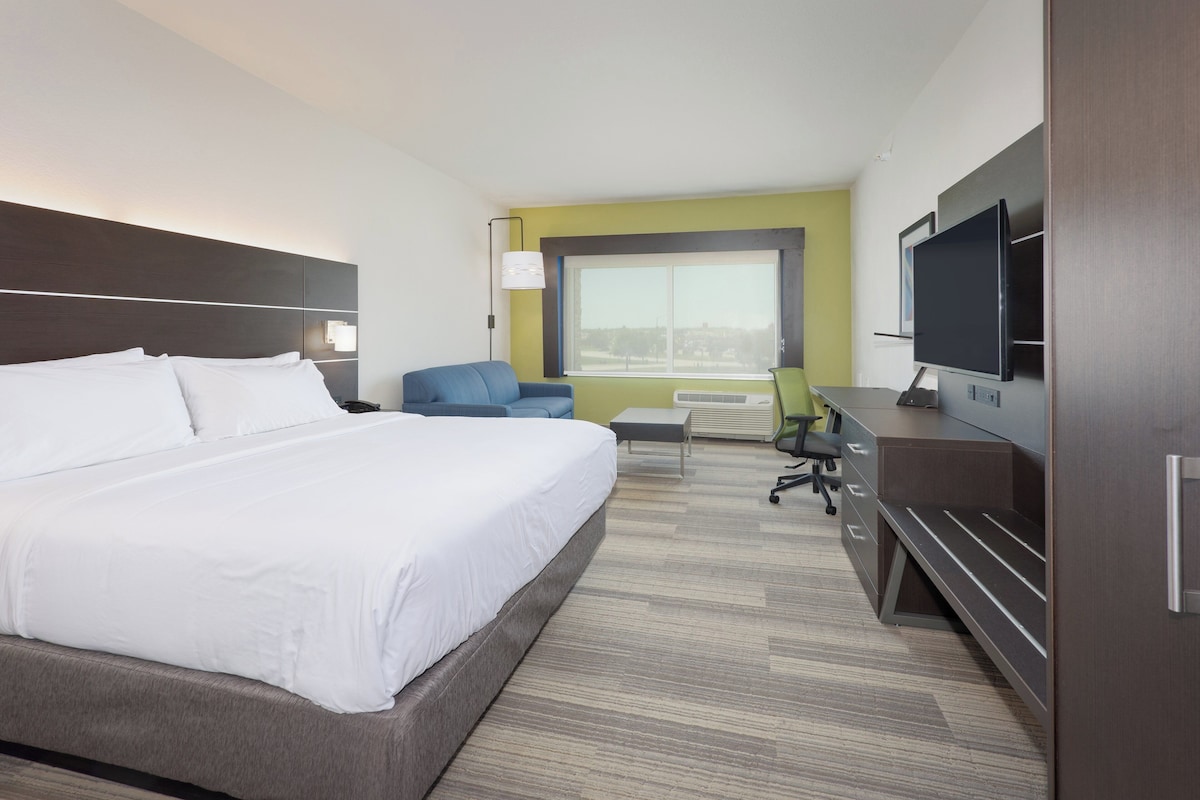 A hotel room with a large bed, a desk with a computer, a chair, and a TV.