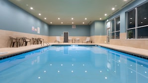 Une piscine intérieure à l’eau claire, entourée de chaises longues et d’une petite table.