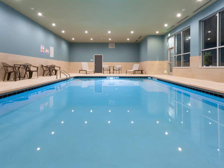 Uma piscina interior com água cristalina, rodeada por espreguiçadeiras e uma pequena mesa.