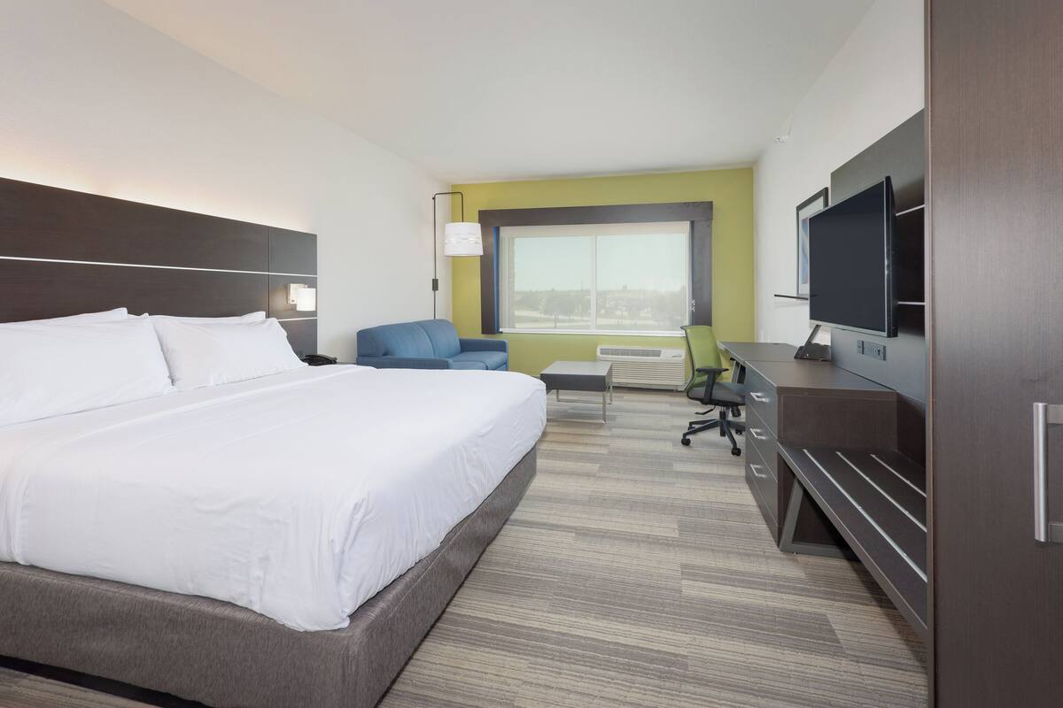 A hotel room with a large bed, a desk with a computer, a chair, and a TV.