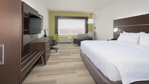 Une chambre d’hôtel avec un grand lit, un bureau avec une chaise, une télévision et une fenêtre donnant sur la ville.