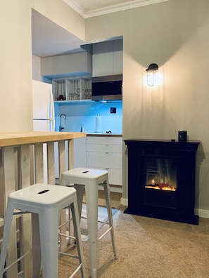 A compact kitchen with a built-in stove, a bar counter, and two stools. - The VICTORIA: Petit Appartment (Elora)