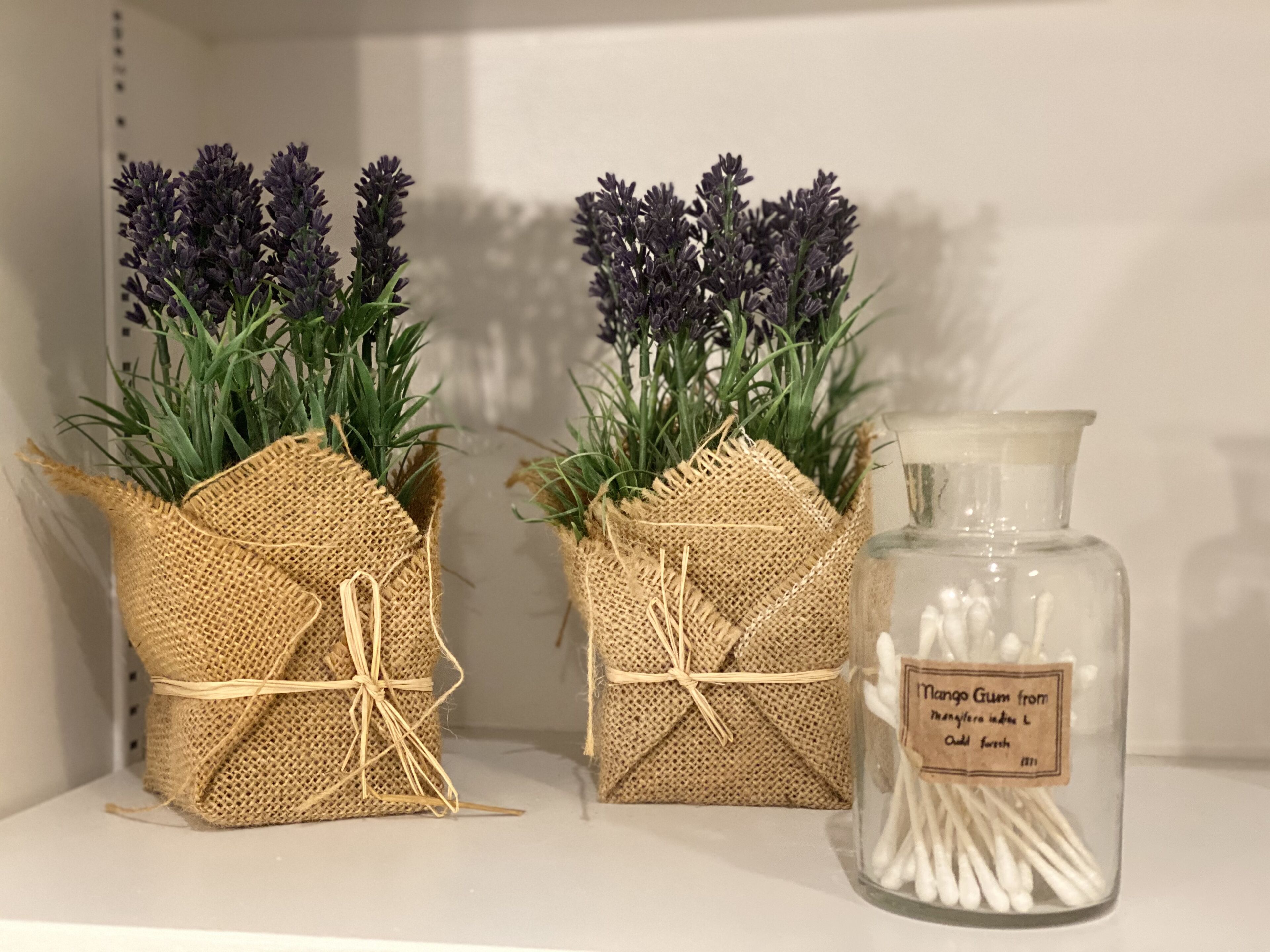 Two burlap-wrapped vases with purple flowers and a glass jar with cotton swabs.