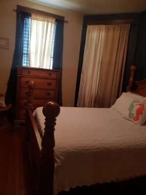 A bedroom with a wooden bed frame, a dresser, and a window with curtains.