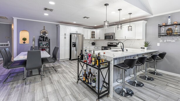 A modern kitchen with white cabinets, a marble island, and a bar area with stools.