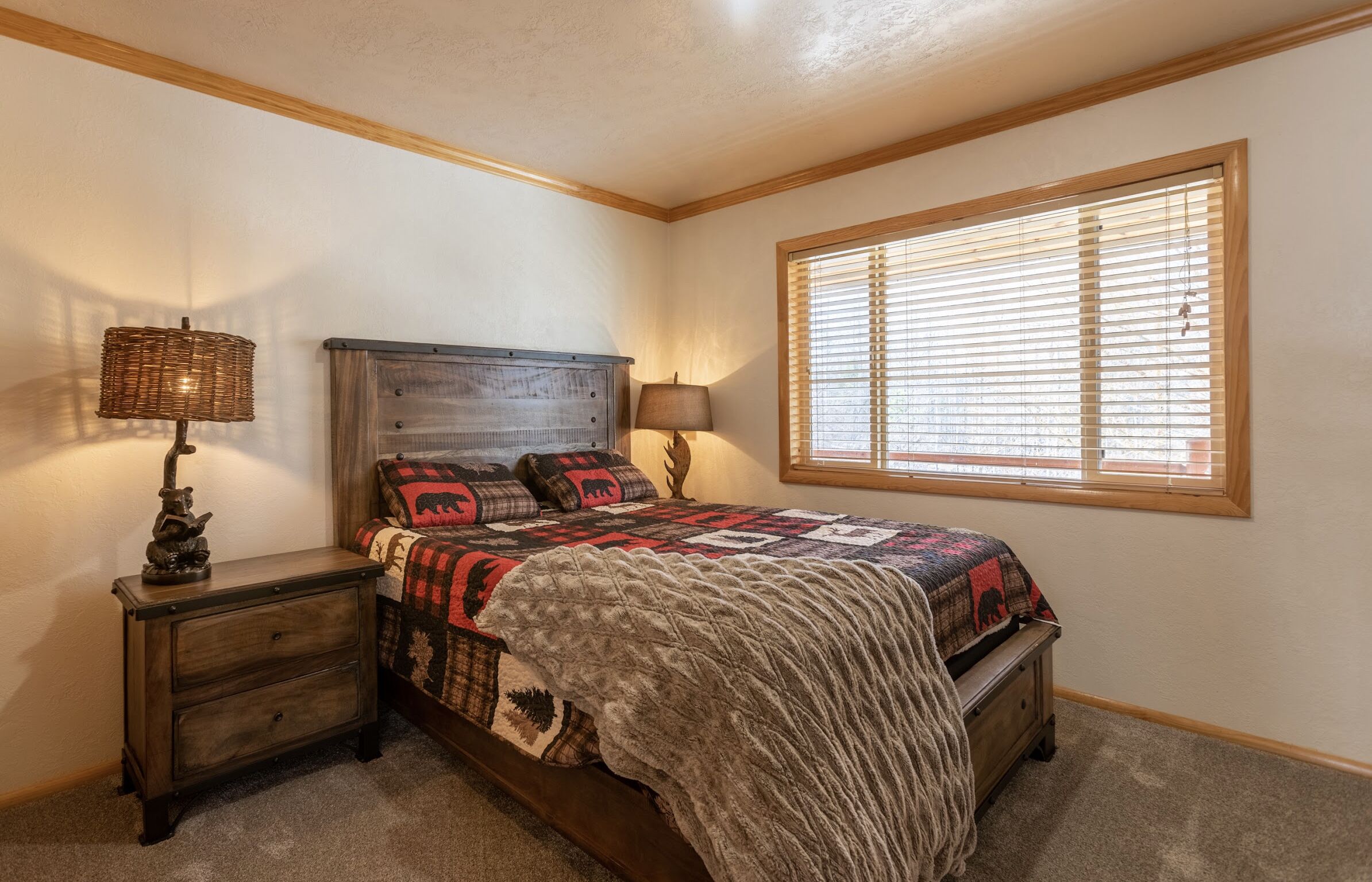 A bedroom with a wooden bed, two nightstands, a window with blinds, and a quilt with animal prints.