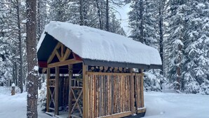 Lumihuntuinen puumökki, jonka katto on peittynyt lumeen, ja jonka ympärillä on lumikuormaisia puita.