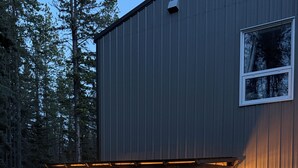 Katettu ulkoalue, jossa on grilli ja valonauhat, ja jota ympäröivät puinen rakennus ja puut.