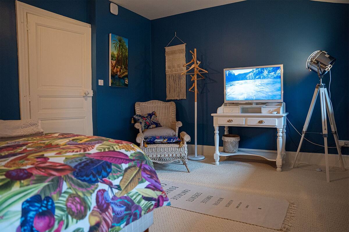 Ein Schlafzimmer mit Bett, Stuhl, Schreibtisch, Fernseher und Stativ.