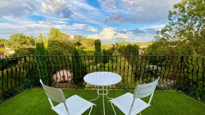 A balcony with a round table and two chairs, surrounded by a metal railing and lush greenery. - Le Rez de Jardin Albi (Albi)