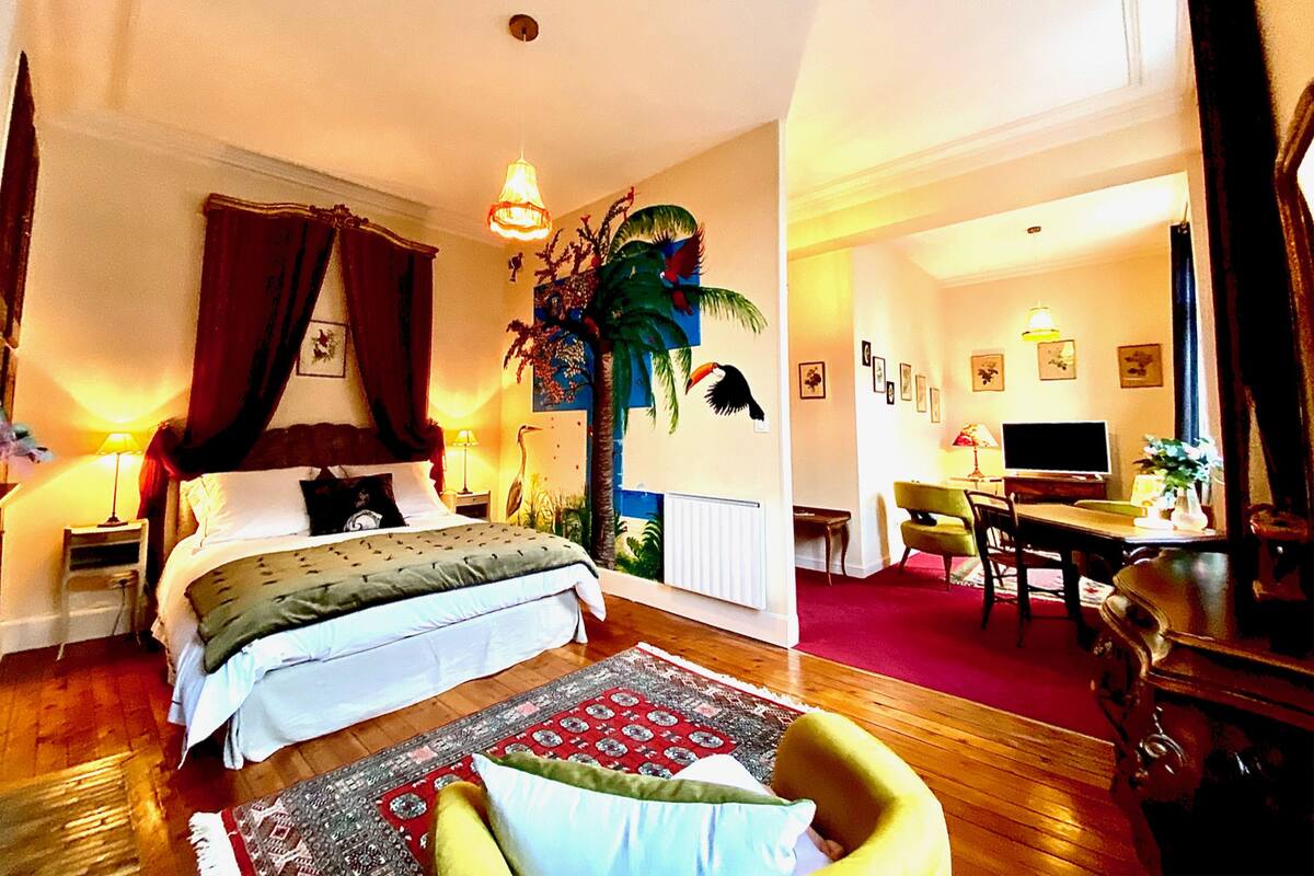 Ein Hotelzimmer mit Bett, Schreibtisch, Sessel, Fernseher und Pflanze.