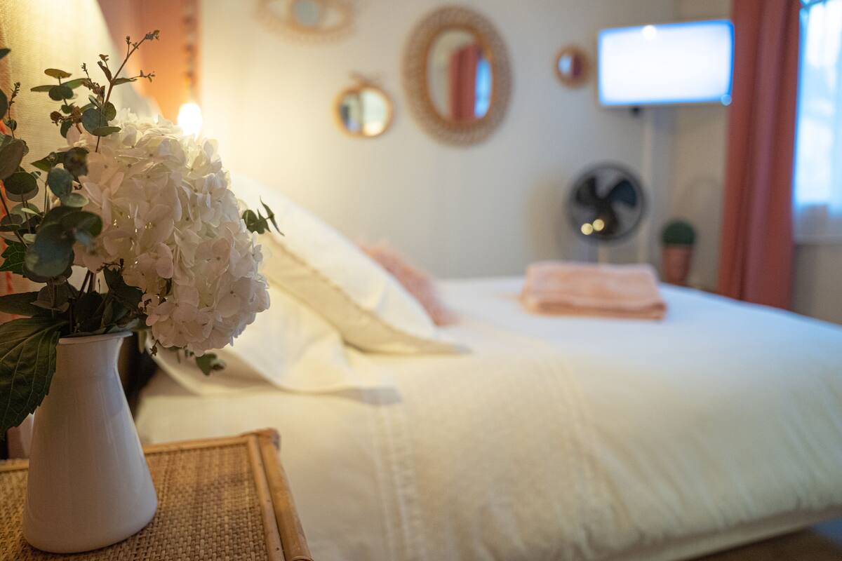 Ein Schlafzimmer mit einem Bett, einer weißen Vase mit Blumen und einem Fernseher an der Wand.