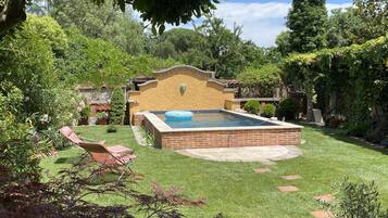 Un patio trasero con piscina, patio de ladrillo y césped.