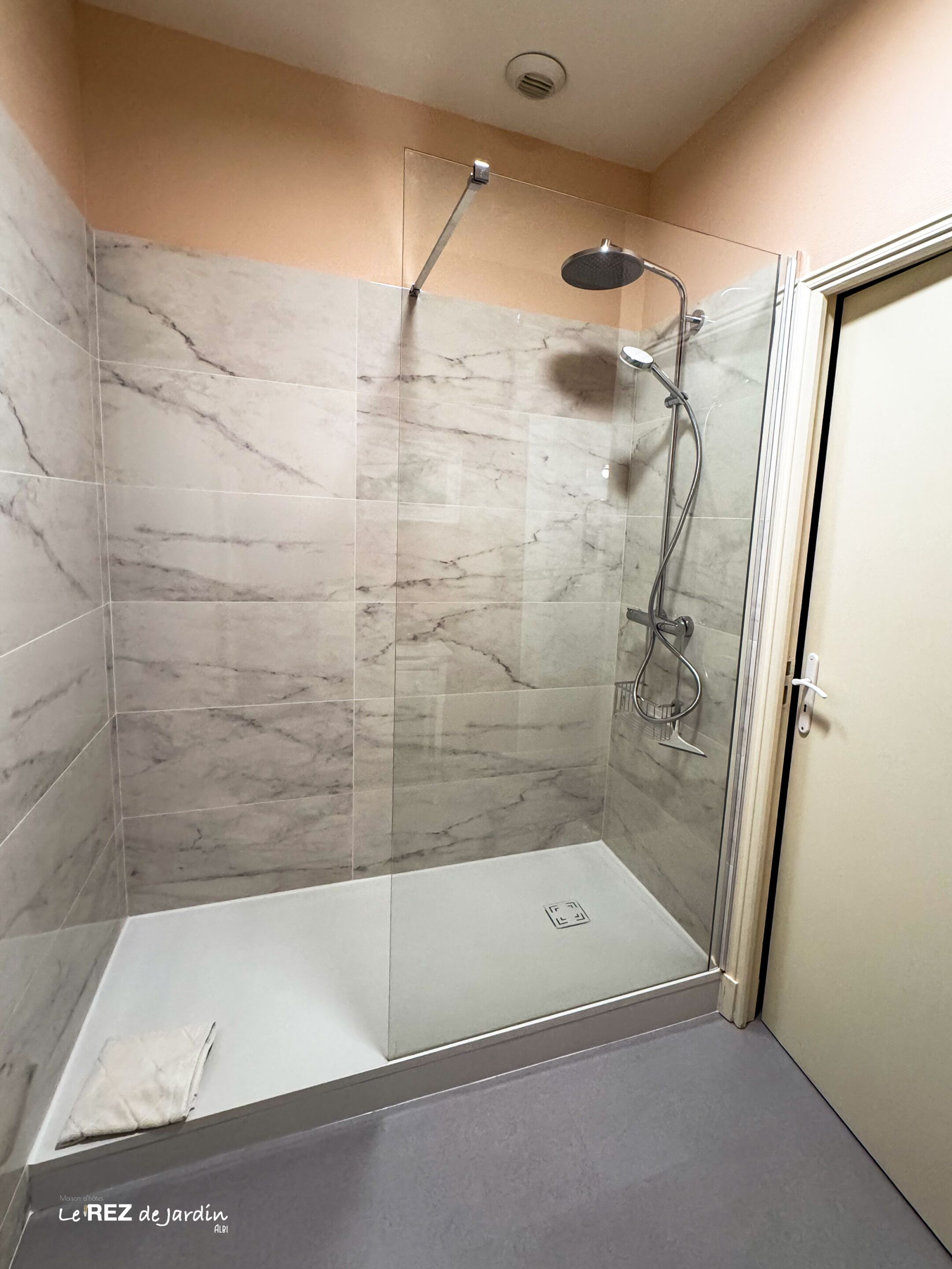Eine begehbare Dusche mit Glastür, Marmorfliesen und Duschkopf.