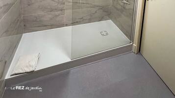 Eine begehbare Dusche mit Glastür, Marmorfliesen und Duschkopf.