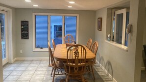 A dining area with a wooden table and chairs, a window with blinds, a wall-mounted phone, and a sign on the wall. - Lakefront Home for Rent (Moultonborough)