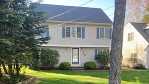 A two-story house with a front yard, a tree, and a well-maintained lawn. - Lakefront Home for Rent (Moultonborough)