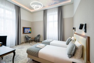 A hotel room with two beds, a desk, a chair, and a painting on the wall.