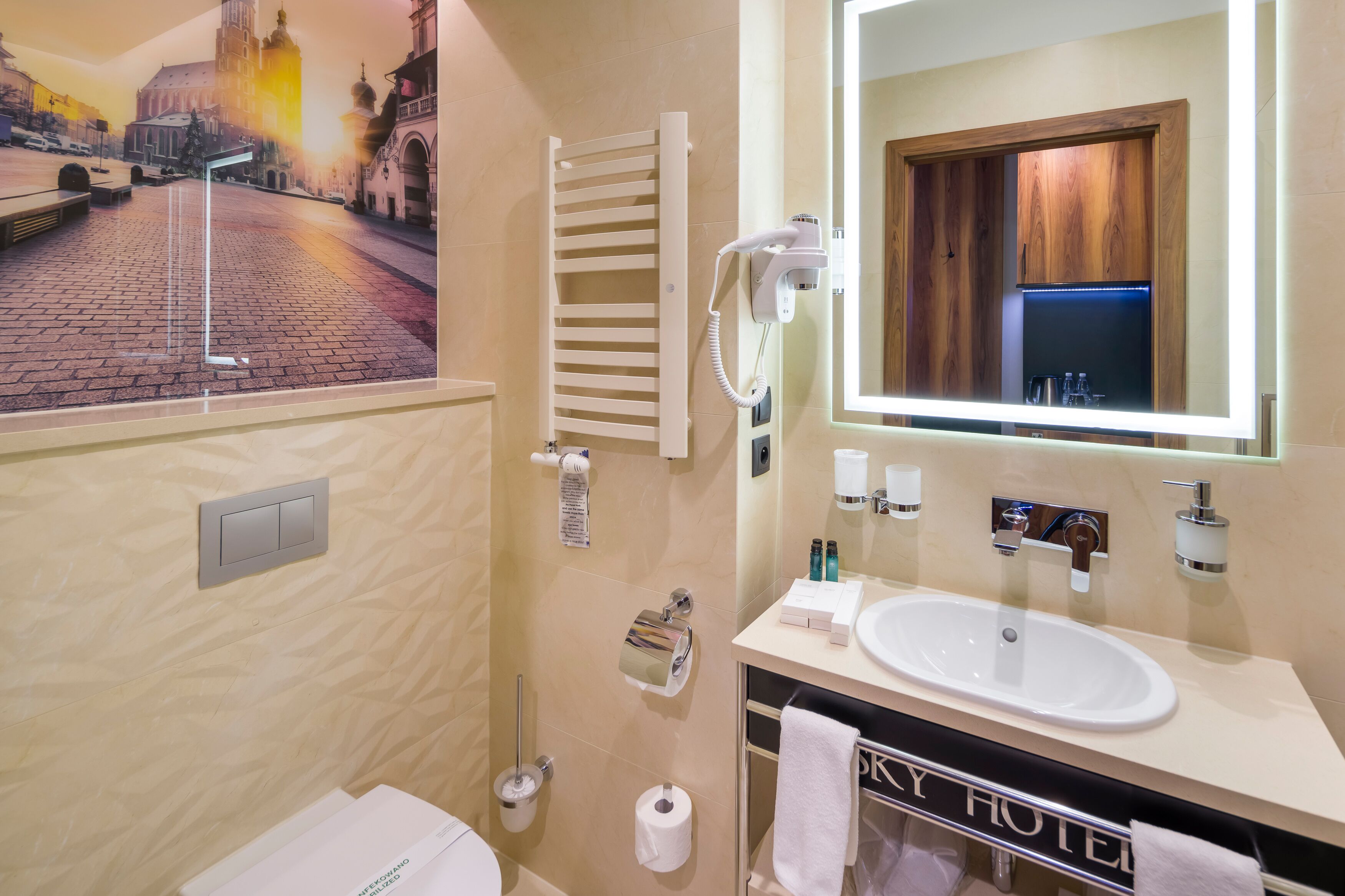 A hotel bathroom with a large mirror, a sink, a towel rack, and a hairdryer.