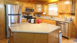 Una cocina con armarios de madera, electrodomésticos de acero inoxidable, encimeras de granito y una isla central.