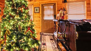 Interior acogedor de una cabaña con un árbol de Navidad decorado, paredes de madera, un sofá de cuero y un techo rústico de madera.