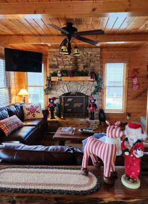 Un intérieur de chalet chaleureux avec une cheminée en pierre, un plafond en bois et un canapé en cuir.
