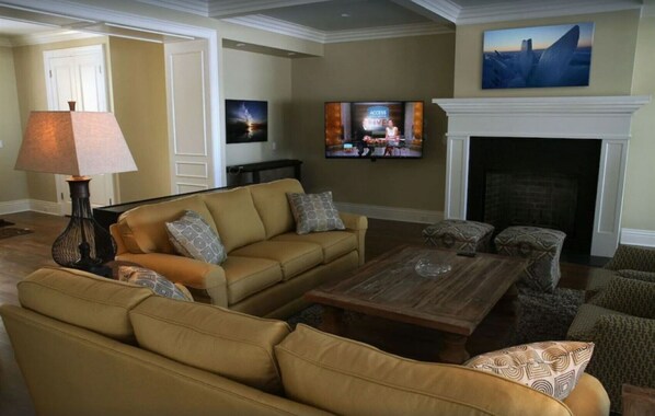Una sala de estar con un sofá, sillones, una mesa de centro, una chimenea y un televisor montado en la pared.